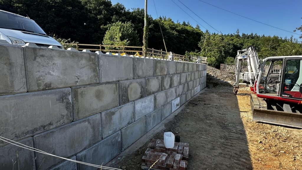 A 16-metre interlocking concrete block retaining wall under construction, with an excavator alongside