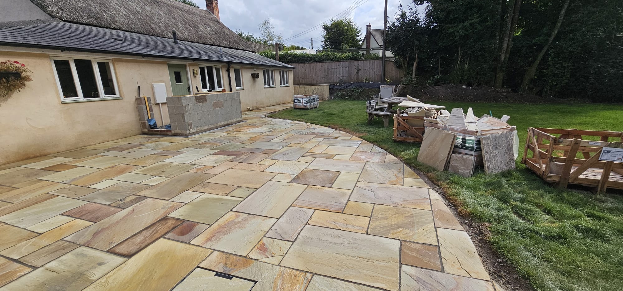 Indian sandstone patio curving in front of the rendered building, with garden furniture on the lawn