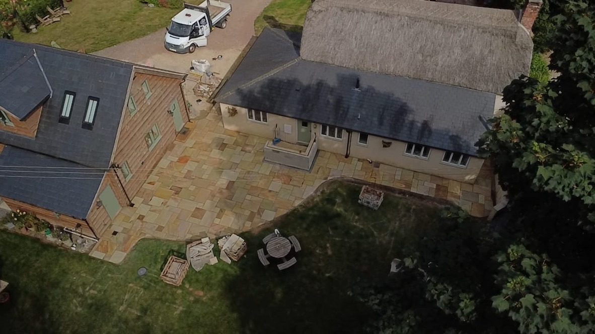 Aerial view of the thatched cottage and extension with sandstone paving wrapping around the building
