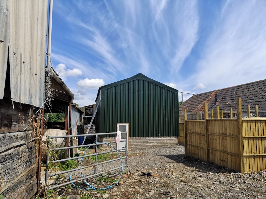 The finished green steel-clad barn seen from the yard, with new timber fencing