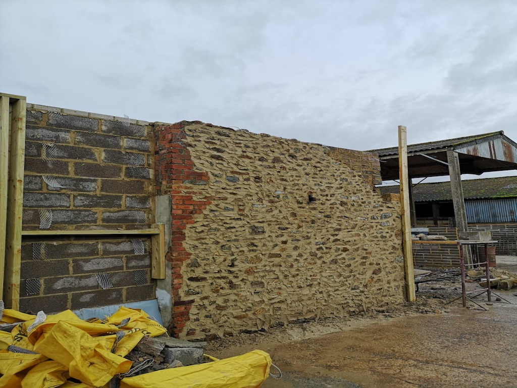 A restored natural stone barn wall with new brick quoins and timber propping