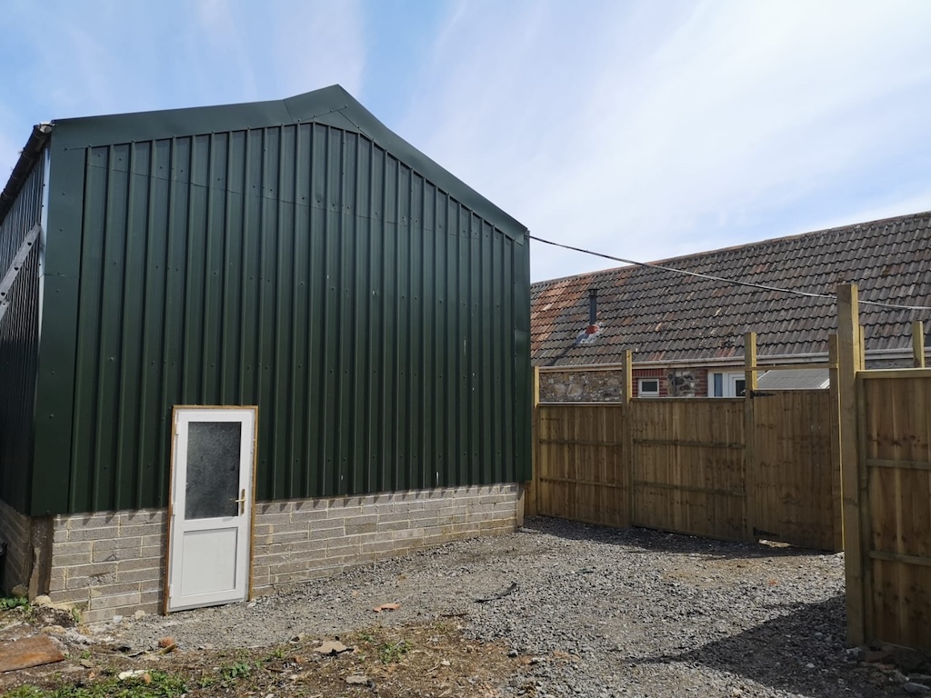 A completed agricultural building clad in green steel sheeting on a blockwork base