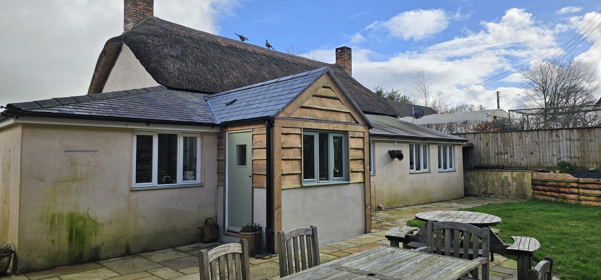 A completed bespoke timber-clad porch on a rendered cottage with a thatched roof